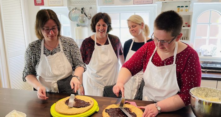 4 Frauen streichen Schokoladenmasse auf Tortenböden